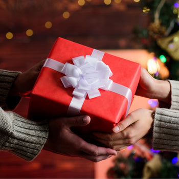two people exchange a wrapped gift in front of holiday decor