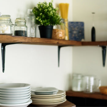 photo of a kitchen corner. dark wood open shelves are above the counter and stocked jars and decor